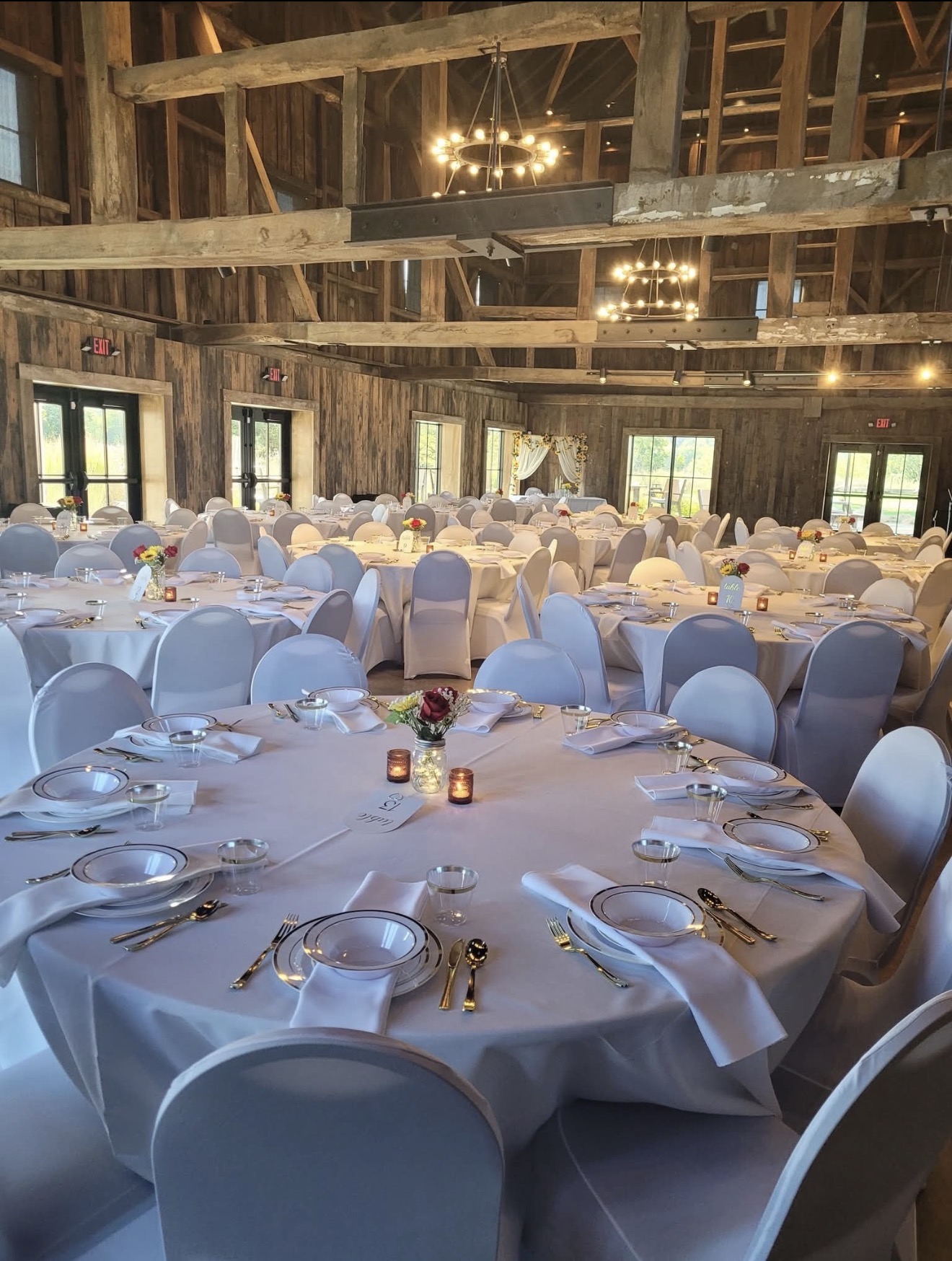 Barn reception with round tables set with white linens, gold flatware and candles