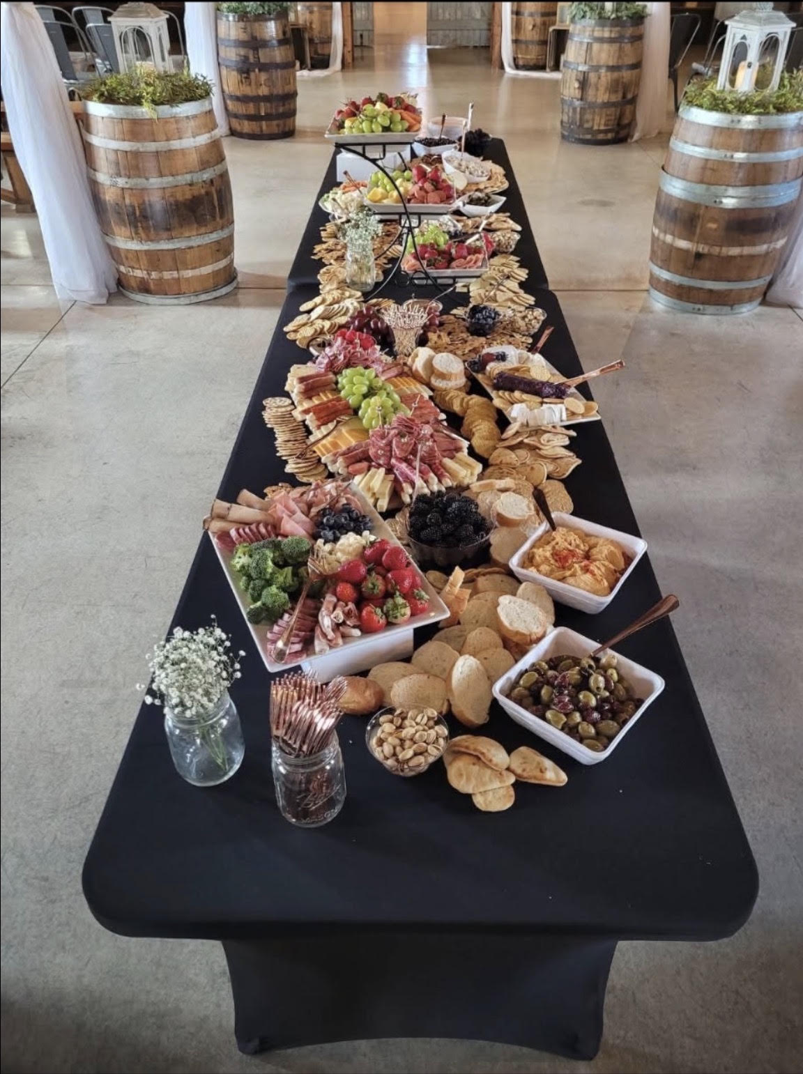 Long black-draped grazing table filled with charcuterie, fruit and crackers in a barn venue