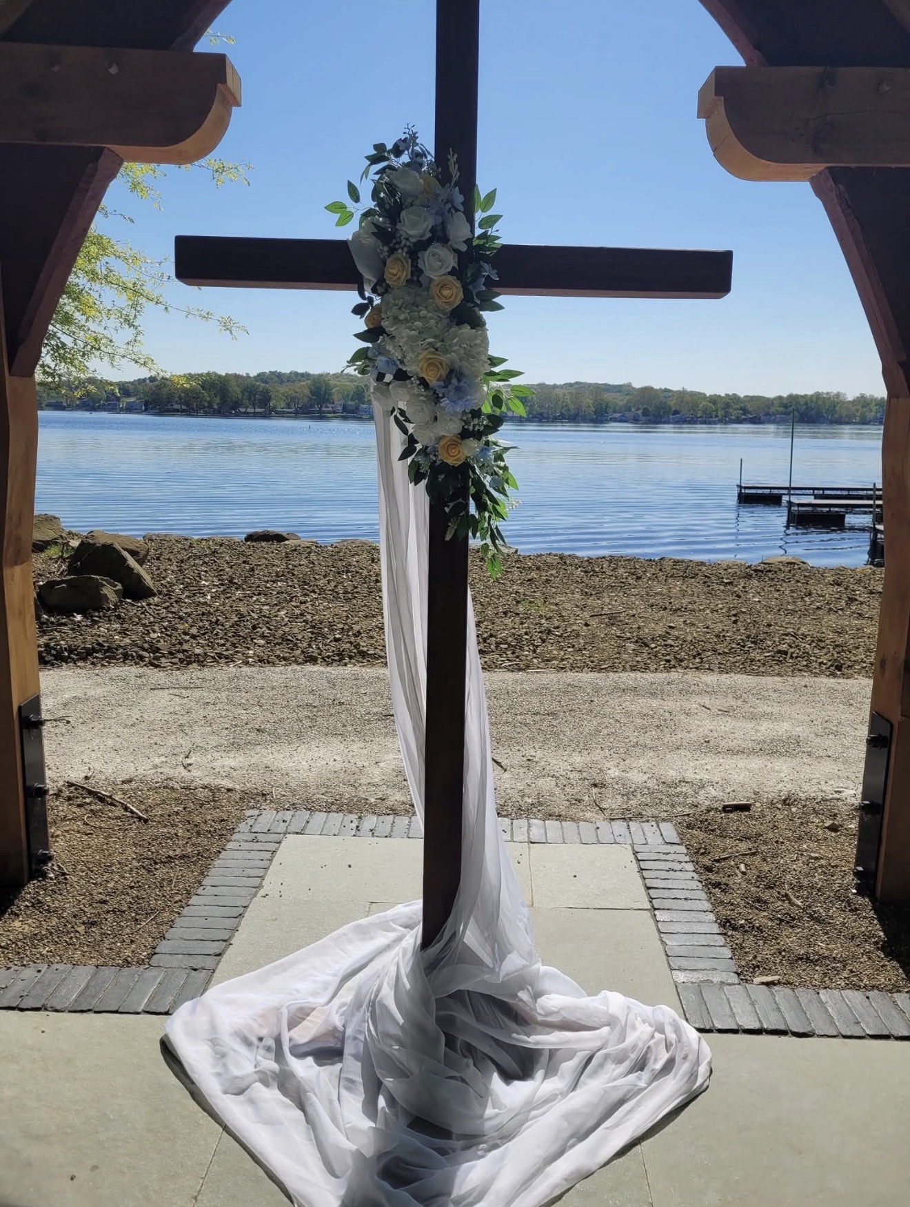 Lakeside ceremony cross draped in white fabric with a floral arrangement